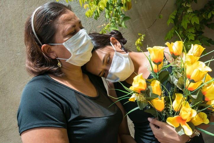 Women mourning those lost to the coronavirus, wearing face masks, showing mutual support, hugging
