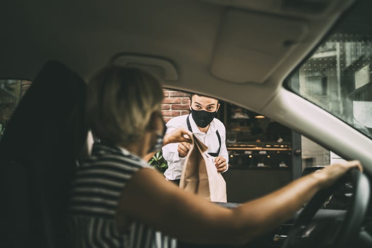 Waiter giving disposable package with food to smiling female driver