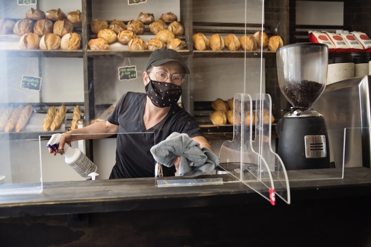 Bakery owner wiping down surfaces wearing mask.
